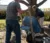 A student scrapes concrete out of a wheelbarrow tipped by a fellow student