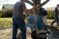 A student scrapes concrete out of a wheelbarrow tipped by a fellow student