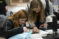 Two female students lean over a tray of samples to analyze them in the lab with a microscope