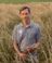 Man standing in field of grain holds onto bunch of it
