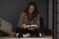 Female student sits pretzel-style on floor studying Bible in low light