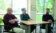 Three professors sit around a table looking at each other