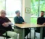 Three professors sit around a table looking at each other