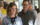 Wife smiles at someone while husband looks on lovingly. Balloons form an arch behind them.