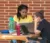 Two females sitting at outdoor table studying on computer laptops with brick wall behind them