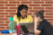Two females sitting at outdoor table studying on computer laptops with brick wall behind them