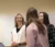 Three female students smile at each other while presenting to the class