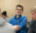 Male student in blue fleece with arms crossed conversing with others in classroom