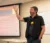 Faculty member stands at the front of the class explaining a concept with arm raised