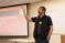 Faculty member stands at the front of the class explaining a concept with arm raised