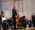 Male cellist stands before the orchestra on stage after completing a solo part