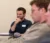 Male smiling student with hand on chin listens at table in class