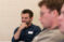 Male smiling student with hand on chin listens at table in class