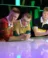 Three young men in rugby shirts lean over counter on stage