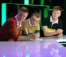 Three young men in rugby shirts lean over counter on stage