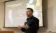 A faculty member stands at the front of a classrom.
