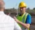 A man in a safety vest and helmet explaining something to another man