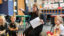 A Teacher sitting down with elementary students pointing at the board