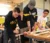 A group of Dordt students with a piece of wood holding it down while one takes a saw to it, working a truss project