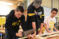 A group of Dordt students with a piece of wood holding it down while one takes a saw to it, working a truss project