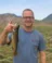 A picture of a man in a grayish-blue shirt holding a fish