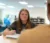 A female student sits with pen raised over notebook as she chats with another student in the library