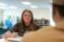 A female student sits with pen raised over notebook as she chats with another student in the library