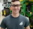 A student wearing safety glasses stands smiling in front of a tractor