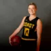 A picture of a smiling women wearing a basketball jersey and posing with a basketball in her hand.